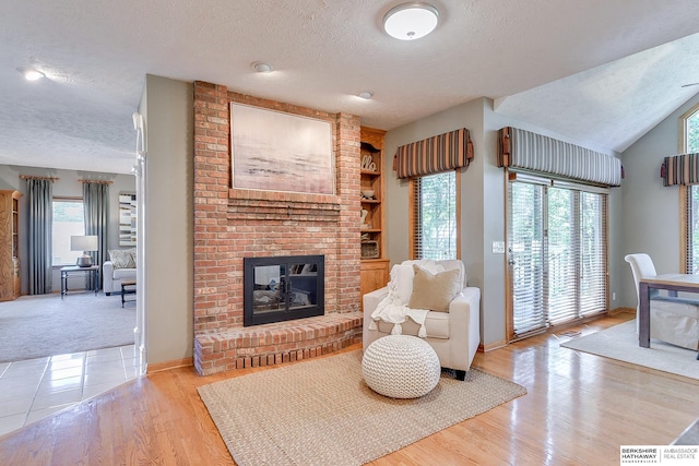 living room featuring a textured ceiling, lofted ceiling, light wood-type flooring, and a fireplace