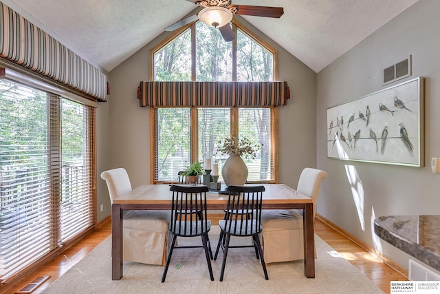 dining space with light hardwood / wood-style flooring, ceiling fan, a textured ceiling, and vaulted ceiling