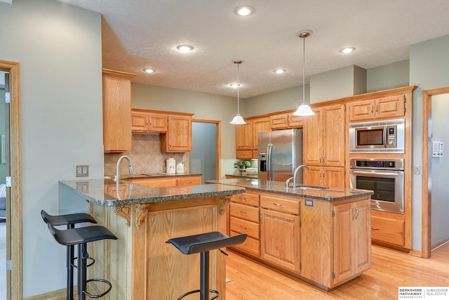 kitchen featuring backsplash, light wood-type flooring, stainless steel appliances, kitchen peninsula, and a kitchen bar