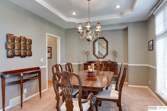 carpeted dining area featuring a tray ceiling and an inviting chandelier