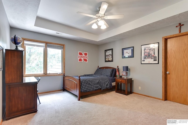 carpeted bedroom featuring ceiling fan and a tray ceiling