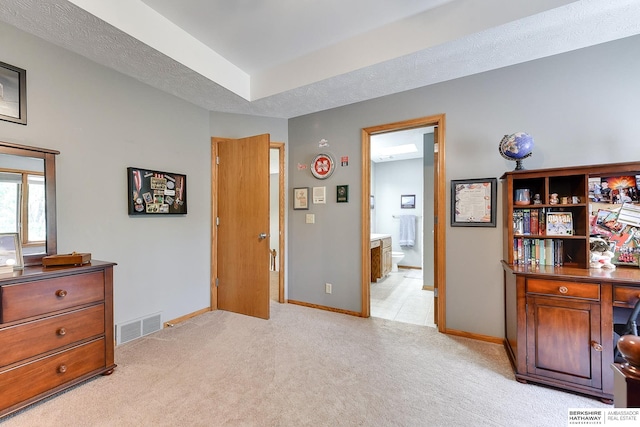 bedroom with a textured ceiling, ensuite bath, and light carpet