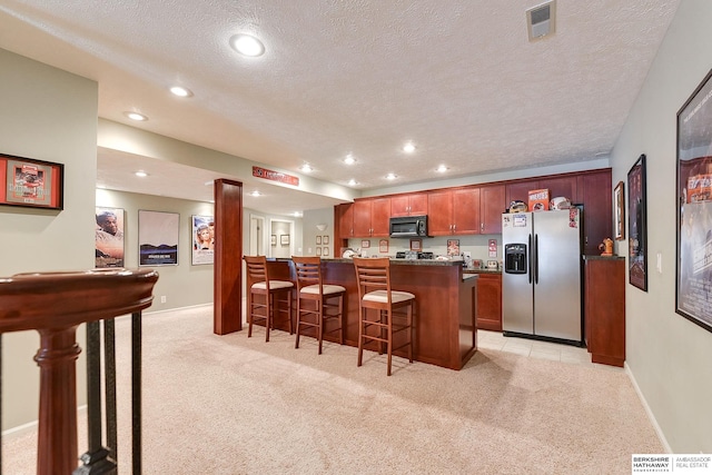 kitchen featuring stainless steel refrigerator with ice dispenser, light carpet, a kitchen bar, and a textured ceiling