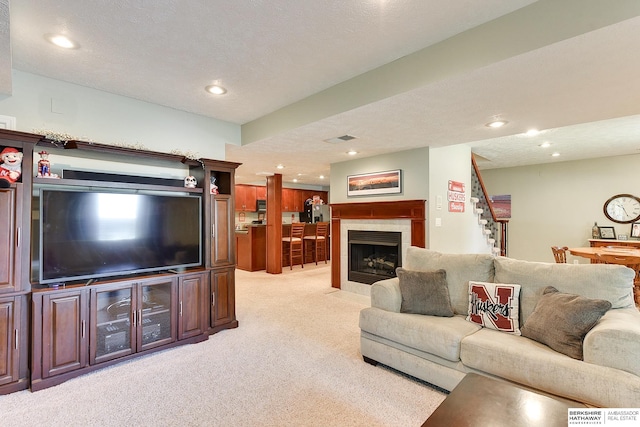 living room with a tiled fireplace, a textured ceiling, and light colored carpet