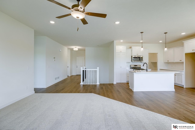 kitchen featuring white cabinetry, ceiling fan, stainless steel appliances, an island with sink, and decorative light fixtures