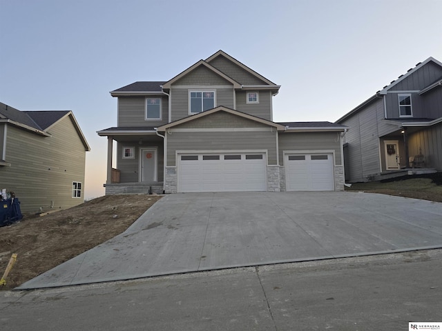 craftsman-style house with stone siding, an attached garage, and driveway