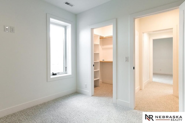 unfurnished bedroom featuring baseboards, visible vents, a walk in closet, and carpet flooring