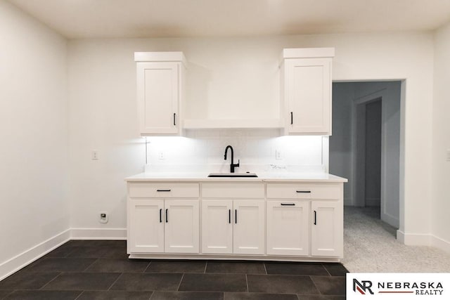 kitchen featuring tasteful backsplash, white cabinetry, a sink, and baseboards