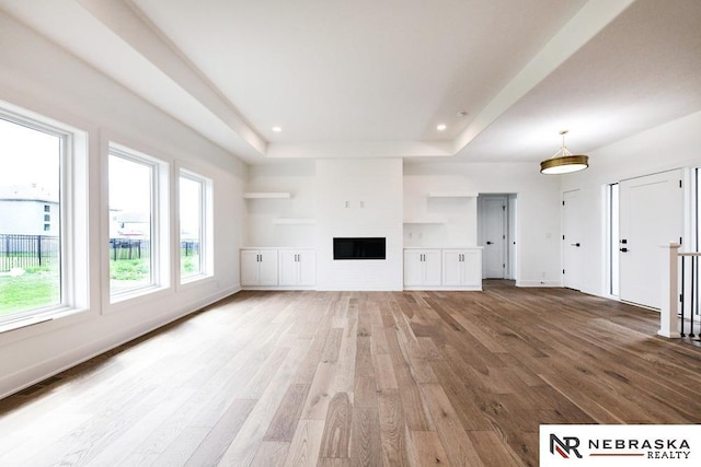 unfurnished living room featuring a fireplace, a tray ceiling, wood finished floors, and recessed lighting