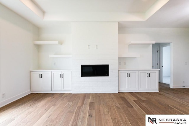 unfurnished living room featuring a fireplace, baseboards, a raised ceiling, and wood finished floors