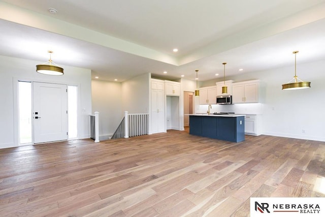 kitchen featuring light wood-style flooring, stainless steel microwave, white cabinets, and open floor plan