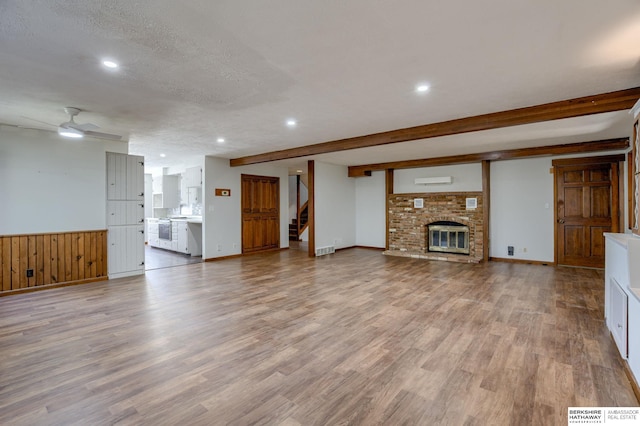 unfurnished living room featuring a fireplace, wood-type flooring, ceiling fan, beam ceiling, and a textured ceiling