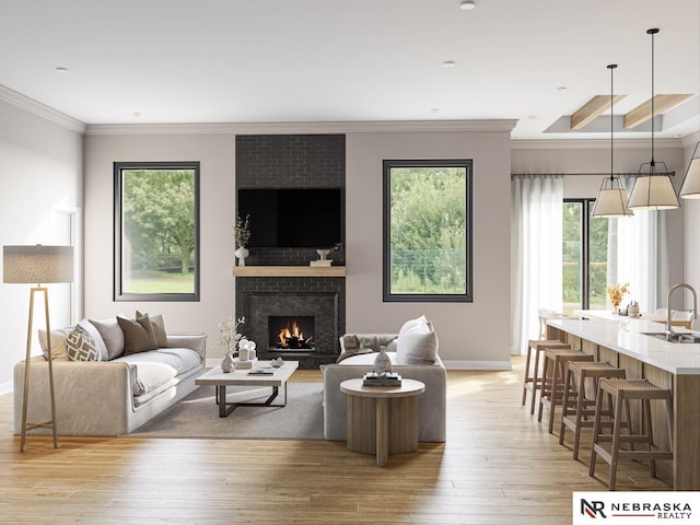 living room with ornamental molding, a fireplace, sink, and light hardwood / wood-style flooring