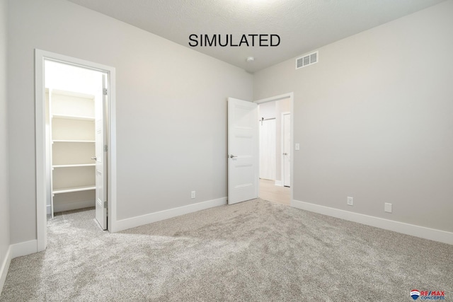 unfurnished bedroom featuring carpet floors, a walk in closet, visible vents, and baseboards