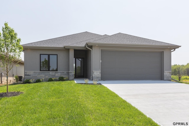 prairie-style house featuring roof with shingles, concrete driveway, a garage, stone siding, and a front lawn