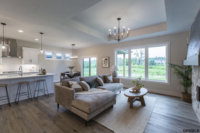 living room with a large fireplace, wood finished floors, baseboards, a raised ceiling, and an inviting chandelier