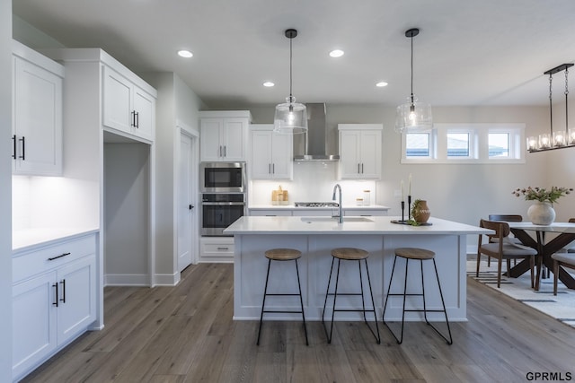 kitchen with appliances with stainless steel finishes, white cabinets, a sink, wood finished floors, and wall chimney exhaust hood