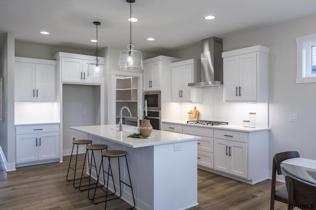 kitchen with dark wood-style flooring, stainless steel microwave, white cabinetry, a sink, and wall chimney exhaust hood