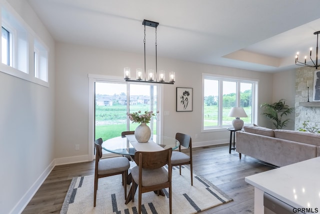 dining space featuring light wood-type flooring, a raised ceiling, a notable chandelier, and baseboards