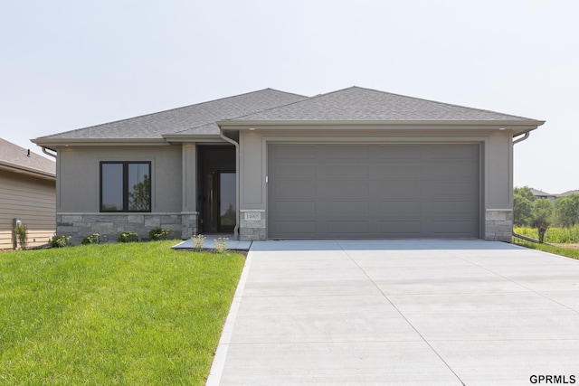 prairie-style home featuring driveway, stone siding, a front yard, and roof with shingles