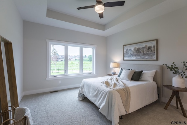 bedroom with carpet floors, a tray ceiling, visible vents, ceiling fan, and baseboards