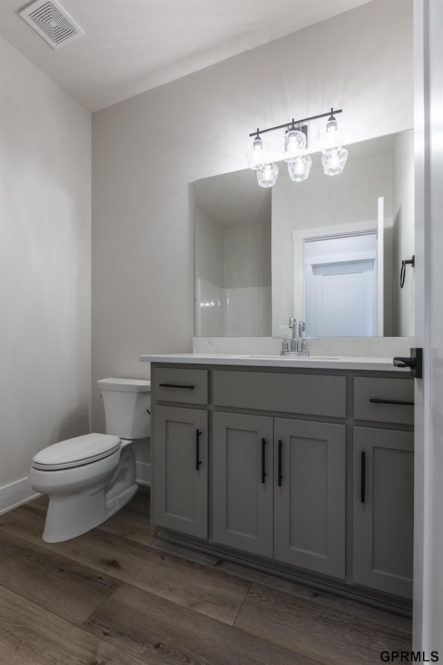 bathroom with visible vents, toilet, vanity, wood finished floors, and baseboards