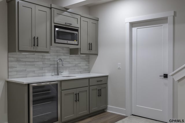 kitchen with beverage cooler, decorative backsplash, stainless steel microwave, gray cabinetry, and a sink