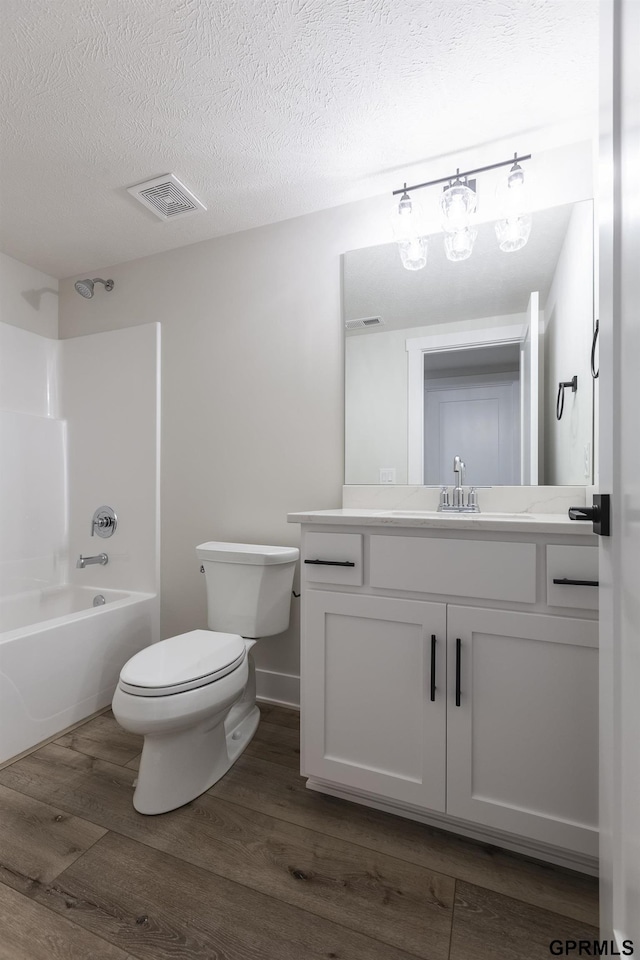 bathroom featuring a textured ceiling, toilet, wood finished floors, visible vents, and shower / bathing tub combination