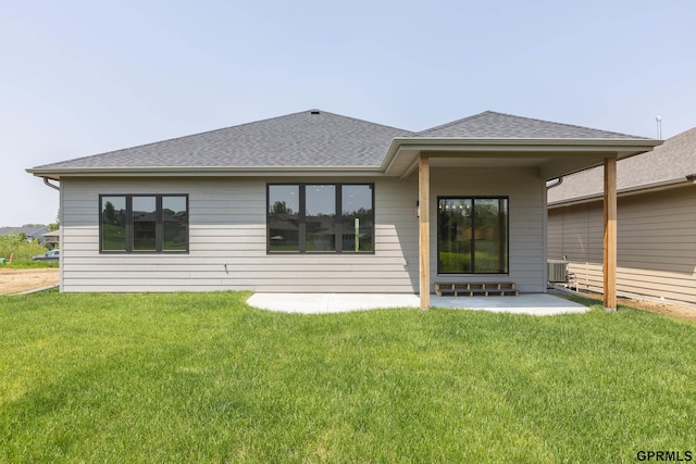 back of property with a yard, a patio area, central AC unit, and roof with shingles