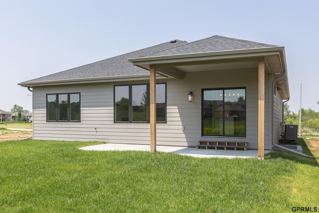 rear view of house featuring a patio area, a lawn, central AC, and roof with shingles