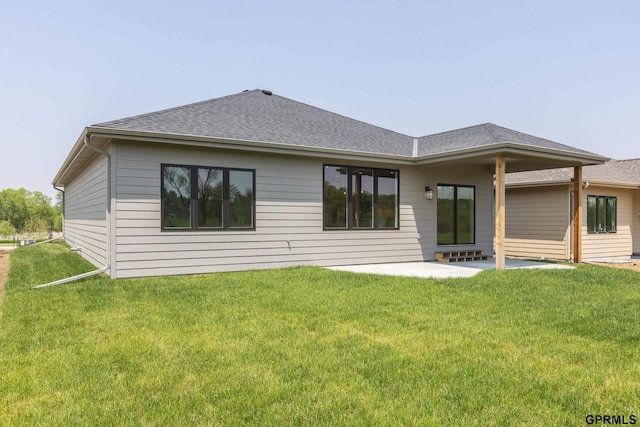 rear view of property featuring a patio, a shingled roof, and a lawn