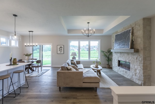 living room with a chandelier, a tray ceiling, a fireplace, and wood finished floors