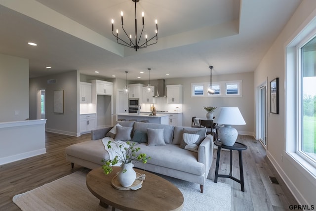 living area with a notable chandelier, a raised ceiling, wood finished floors, and recessed lighting