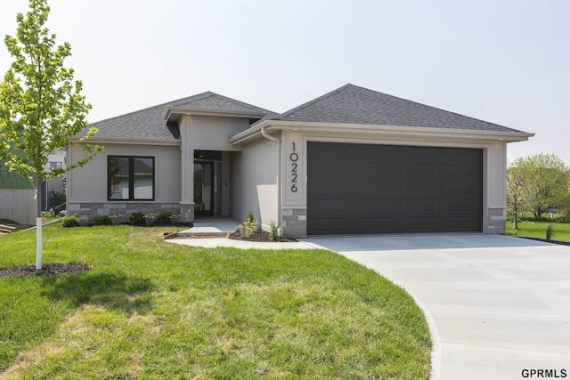 prairie-style house featuring a garage, a shingled roof, stone siding, driveway, and a front yard