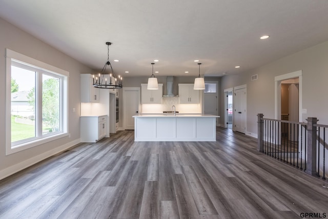 kitchen featuring light countertops, white cabinets, an island with sink, wood finished floors, and wall chimney exhaust hood