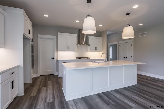 kitchen featuring visible vents, dark wood-style floors, light countertops, wall chimney range hood, and a sink