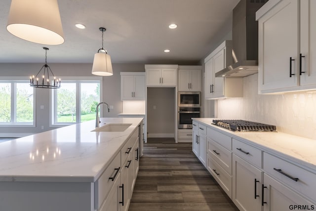 kitchen with wall chimney range hood, white cabinetry, appliances with stainless steel finishes, and a sink