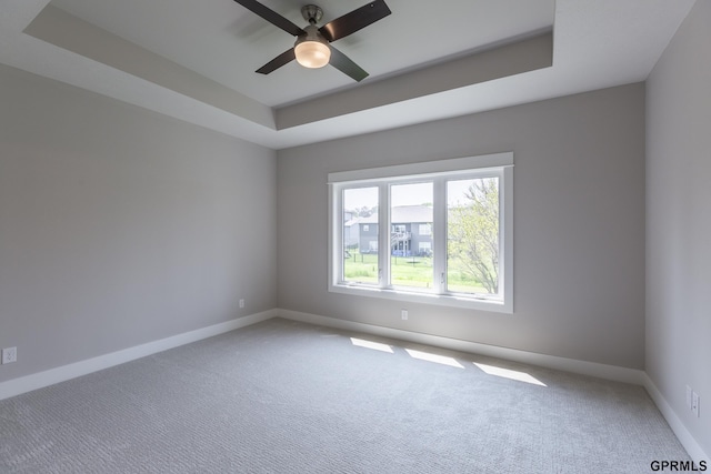 carpeted empty room featuring ceiling fan, baseboards, and a raised ceiling