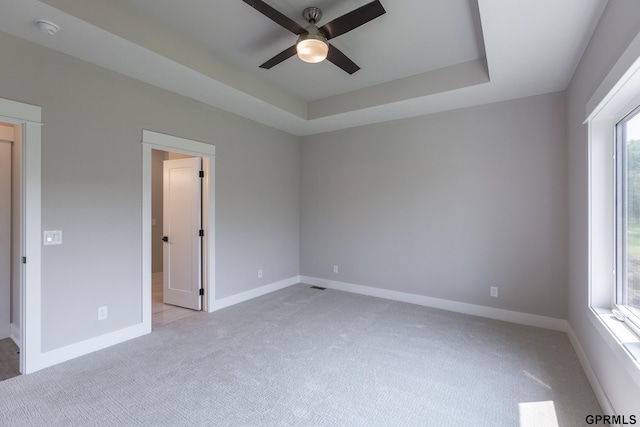 unfurnished room featuring light carpet, ceiling fan, a tray ceiling, and baseboards