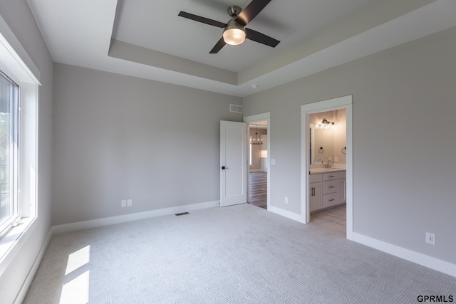 unfurnished bedroom with light colored carpet, a sink, visible vents, baseboards, and a raised ceiling