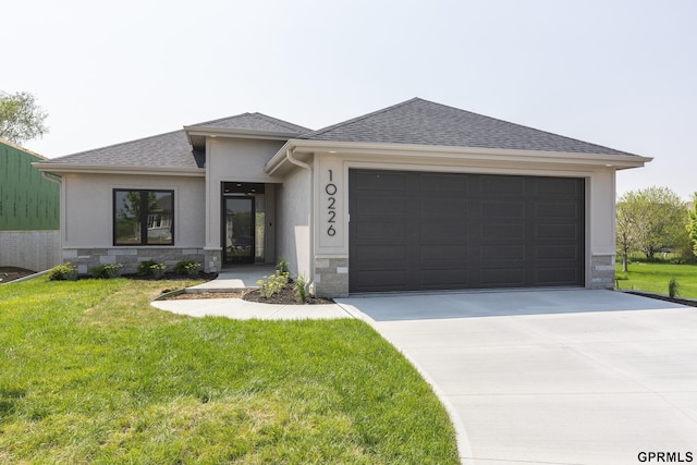 prairie-style home with a front yard, stone siding, roof with shingles, and driveway