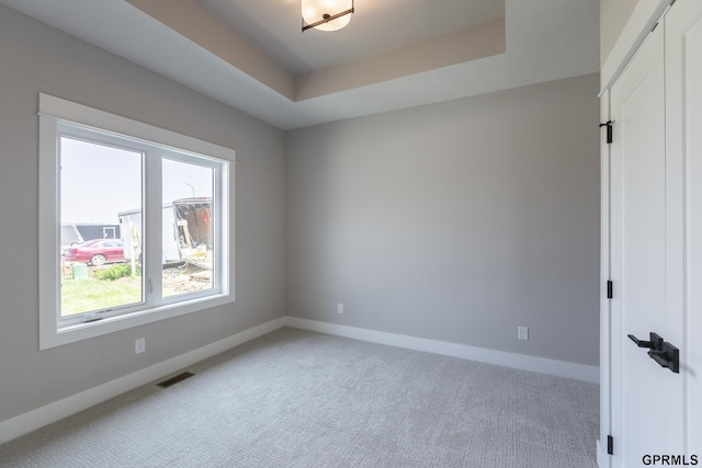 carpeted spare room featuring baseboards, visible vents, and a raised ceiling