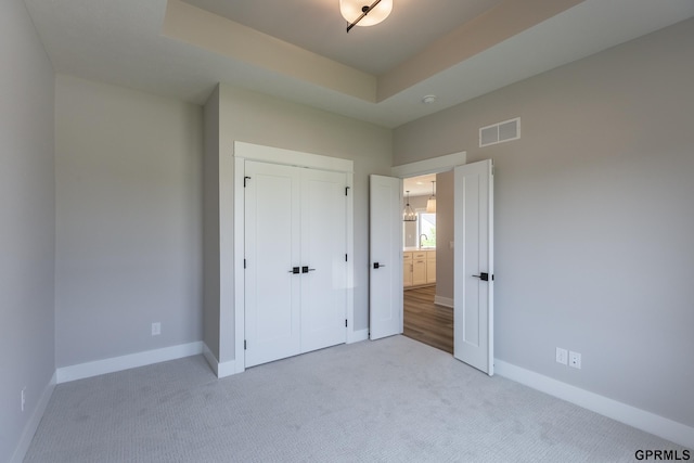 unfurnished bedroom with carpet, a closet, a raised ceiling, visible vents, and baseboards