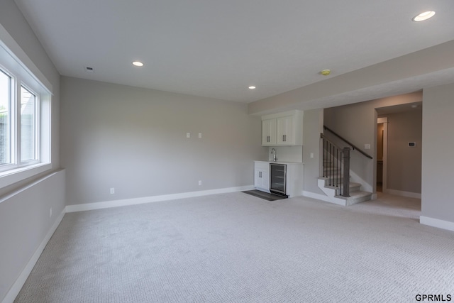 unfurnished living room featuring light carpet, beverage cooler, stairway, indoor wet bar, and recessed lighting