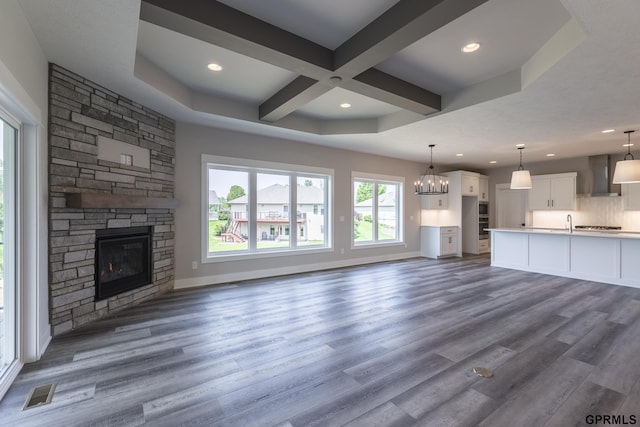 unfurnished living room with a stone fireplace, dark wood finished floors, visible vents, and baseboards