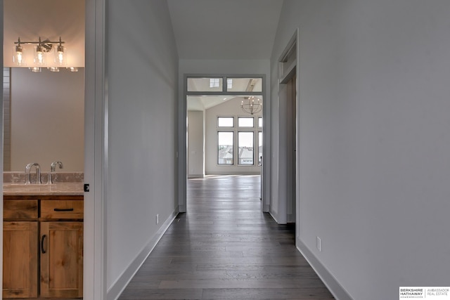 corridor with vaulted ceiling, dark hardwood / wood-style floors, sink, and a notable chandelier