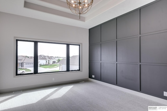 unfurnished bedroom with light colored carpet, a notable chandelier, and a tray ceiling