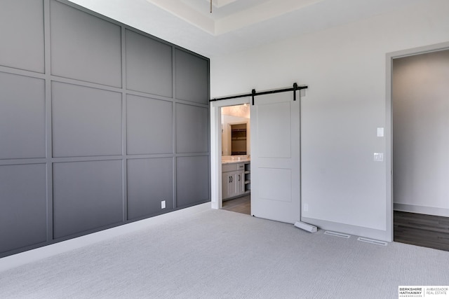 unfurnished bedroom featuring light wood-type flooring, ensuite bath, and a barn door