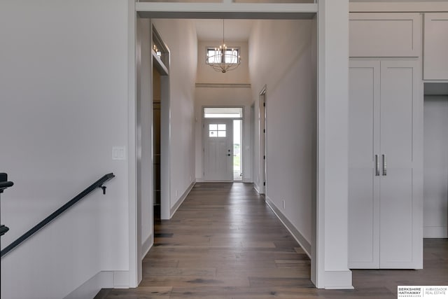 corridor with an inviting chandelier, a towering ceiling, and dark wood-type flooring