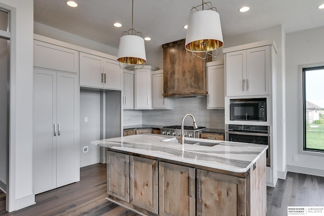 kitchen with light stone counters, white cabinets, a center island with sink, oven, and black microwave